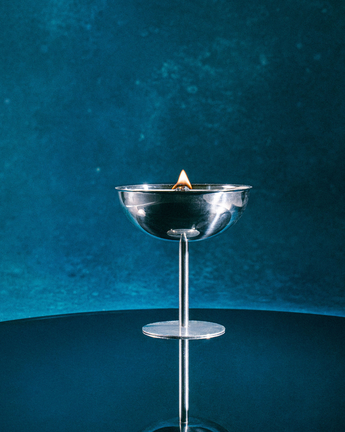 Célébration candle burning in its stainless steel champagne cup, wooden wick flame on a deep blue background