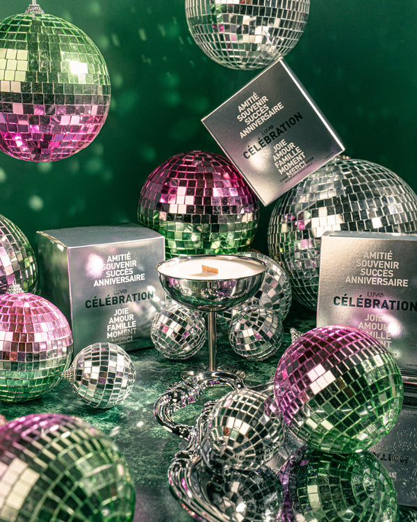 Célébration candle by LUVO in a silver champagne coupe with its silver gift boxes among pink and green disco balls