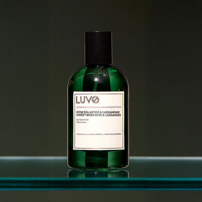 Sweet Brier Rose & Cardamom eau de parfum 100ml in a refillable green glass bottle on a glass shelf